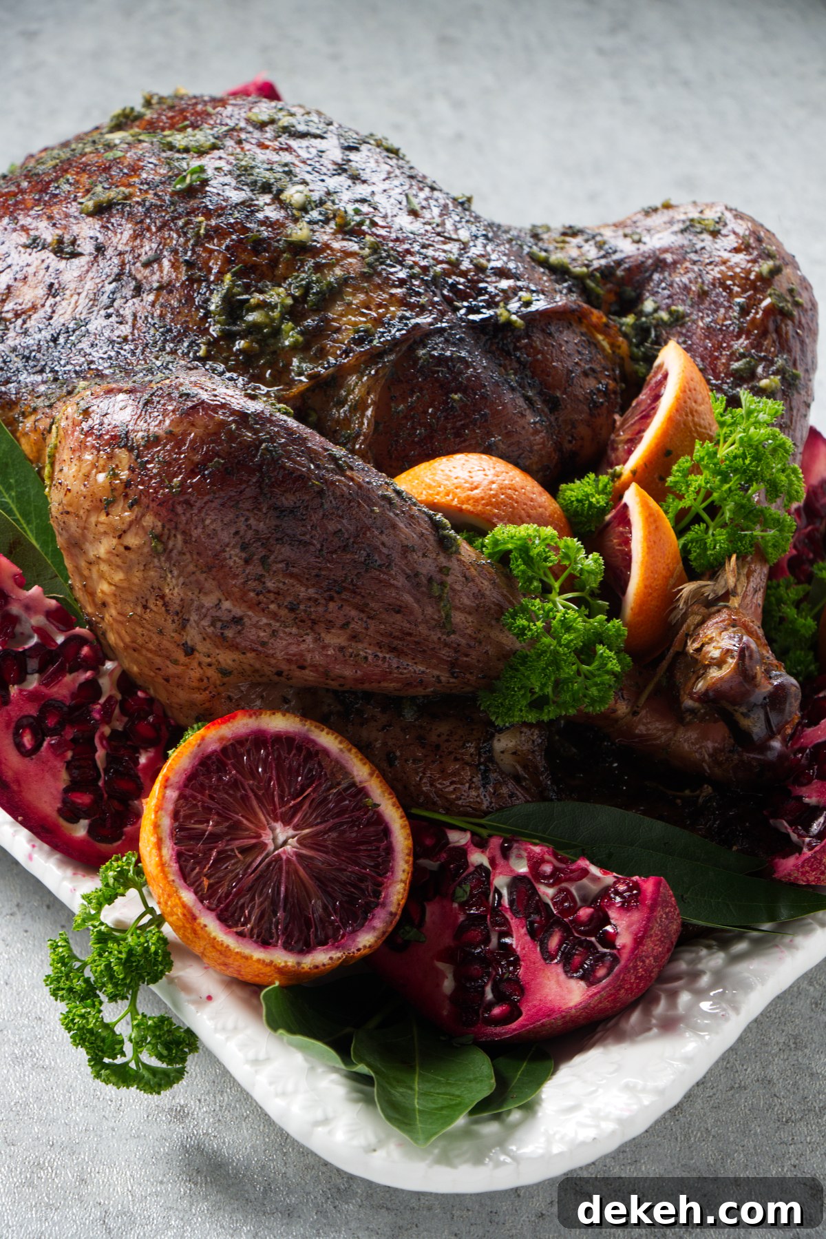 Whole dry brine smoked turkey on a platter arranged with citrus, pomegranate, and herbs as garnish.