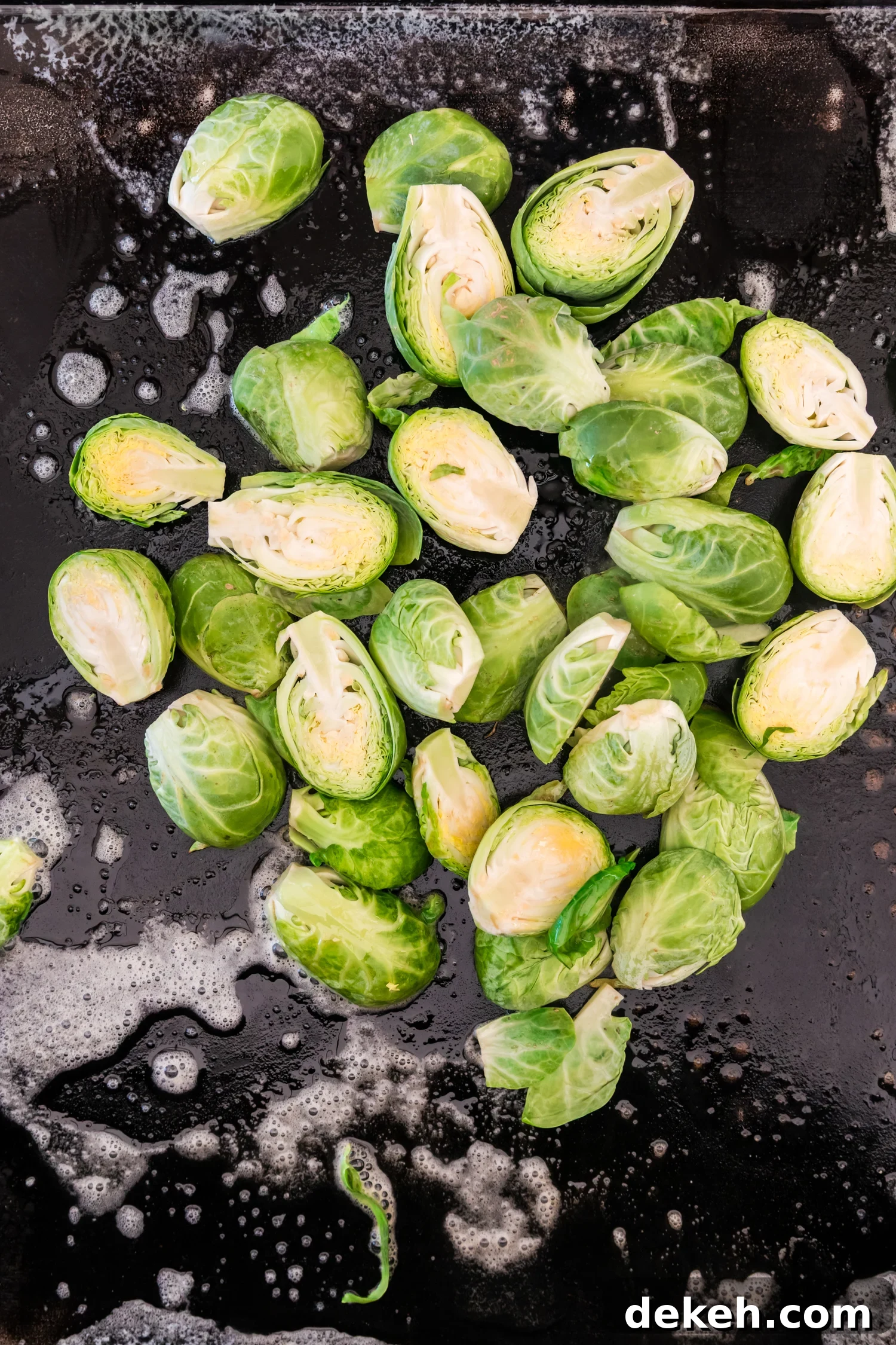 Halved Brussels sprouts placed on a hot griddle surface, beginning to cook in melted butter.