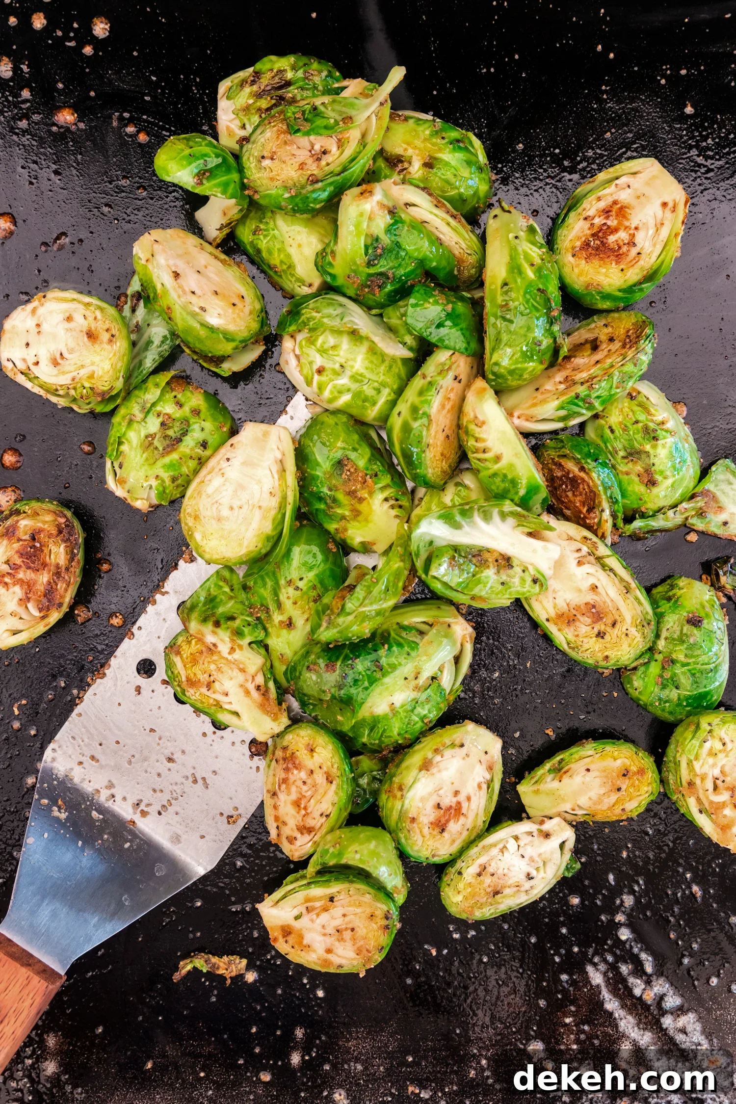 Brussels sprouts cooking on a flat-top grill, starting to brown slightly with a spatula nearby.