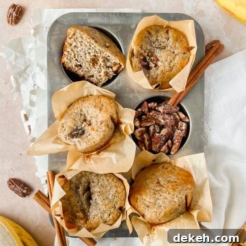 baked greek yogurt banana muffins baked in parchment liners arranged in a 6 muffin muffin tin with pecans, cinnamon sticks, and bananas surrounding.