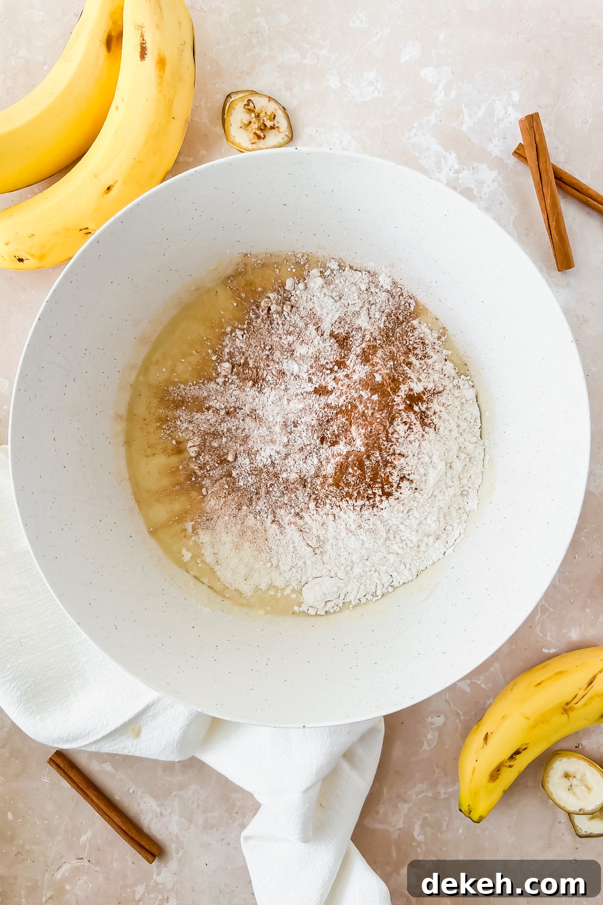 wet ingredients for greek yogurt banana muffins mixed in white mixing bowl with flour and cinnamon added on top.