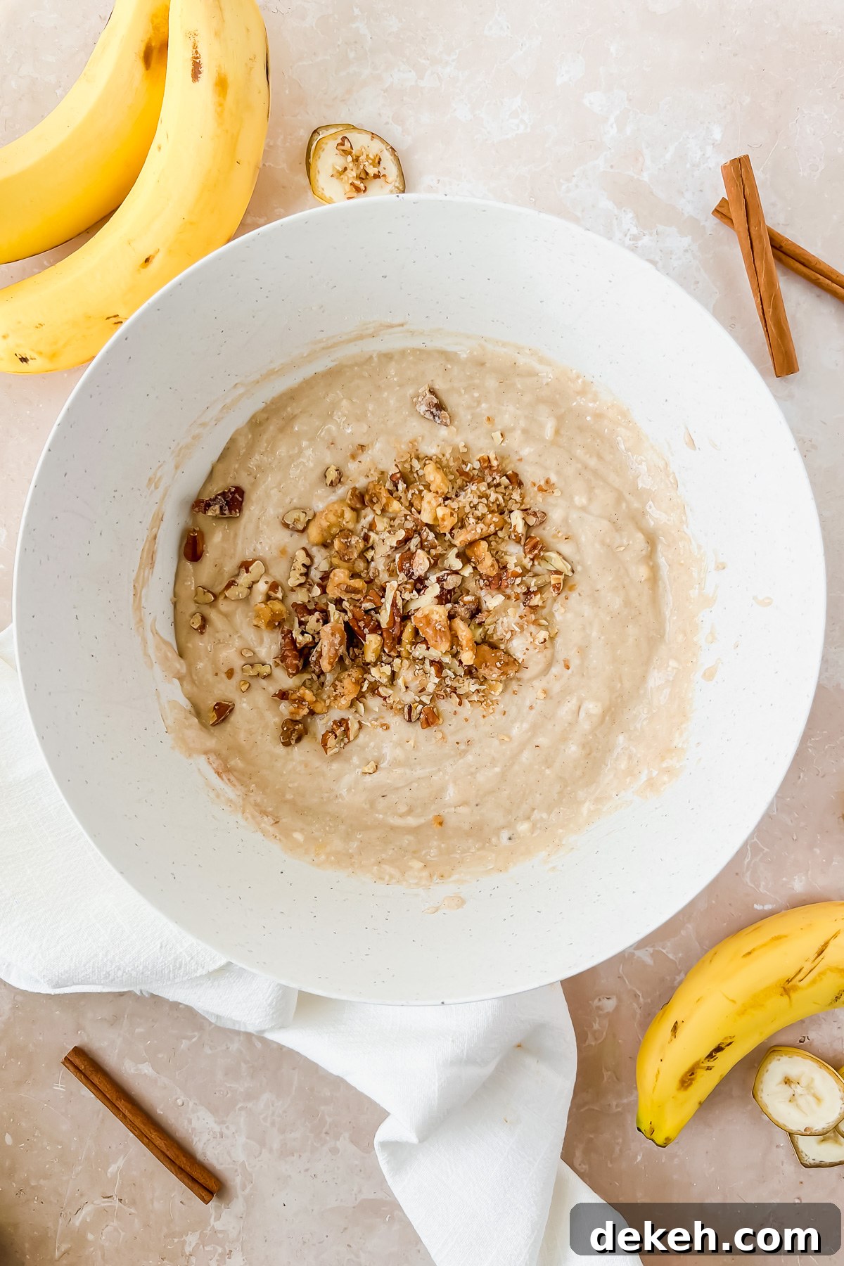greek yogurt banana muffin batter in mixed in white mixing bowl with chopped nuts added on top.