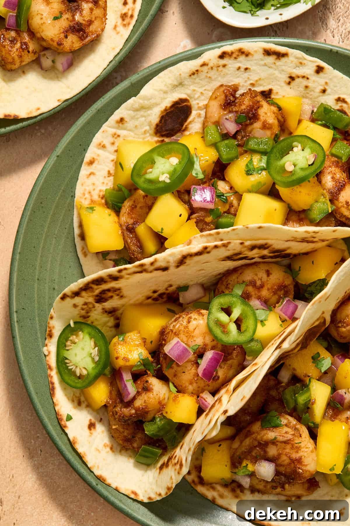 View of tortillas with spicy shrimp and mango salsa on top on green plate.