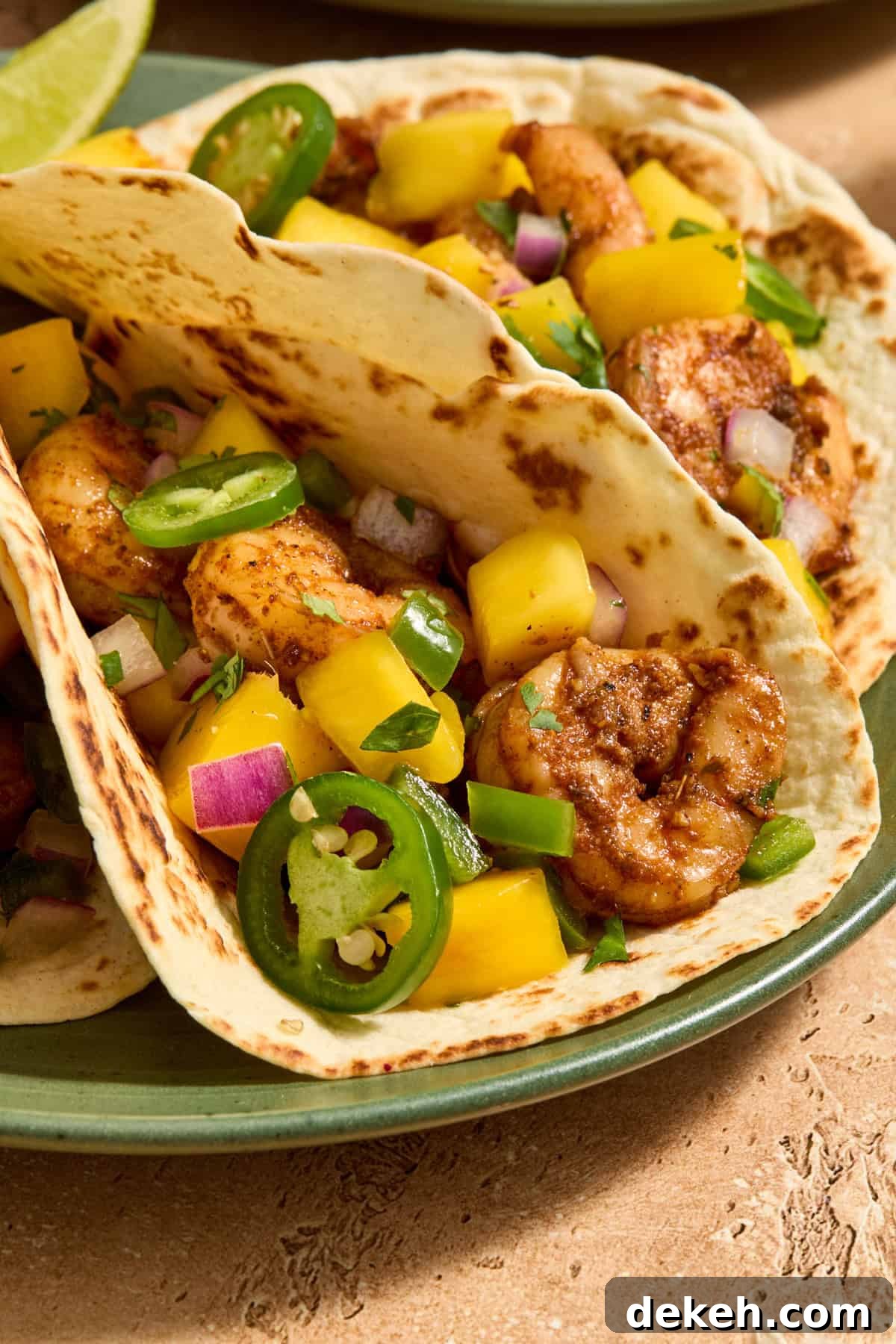 Spicy shrimp tacos on plate topped with mango salsa, cilantro and sliced jalapeños.