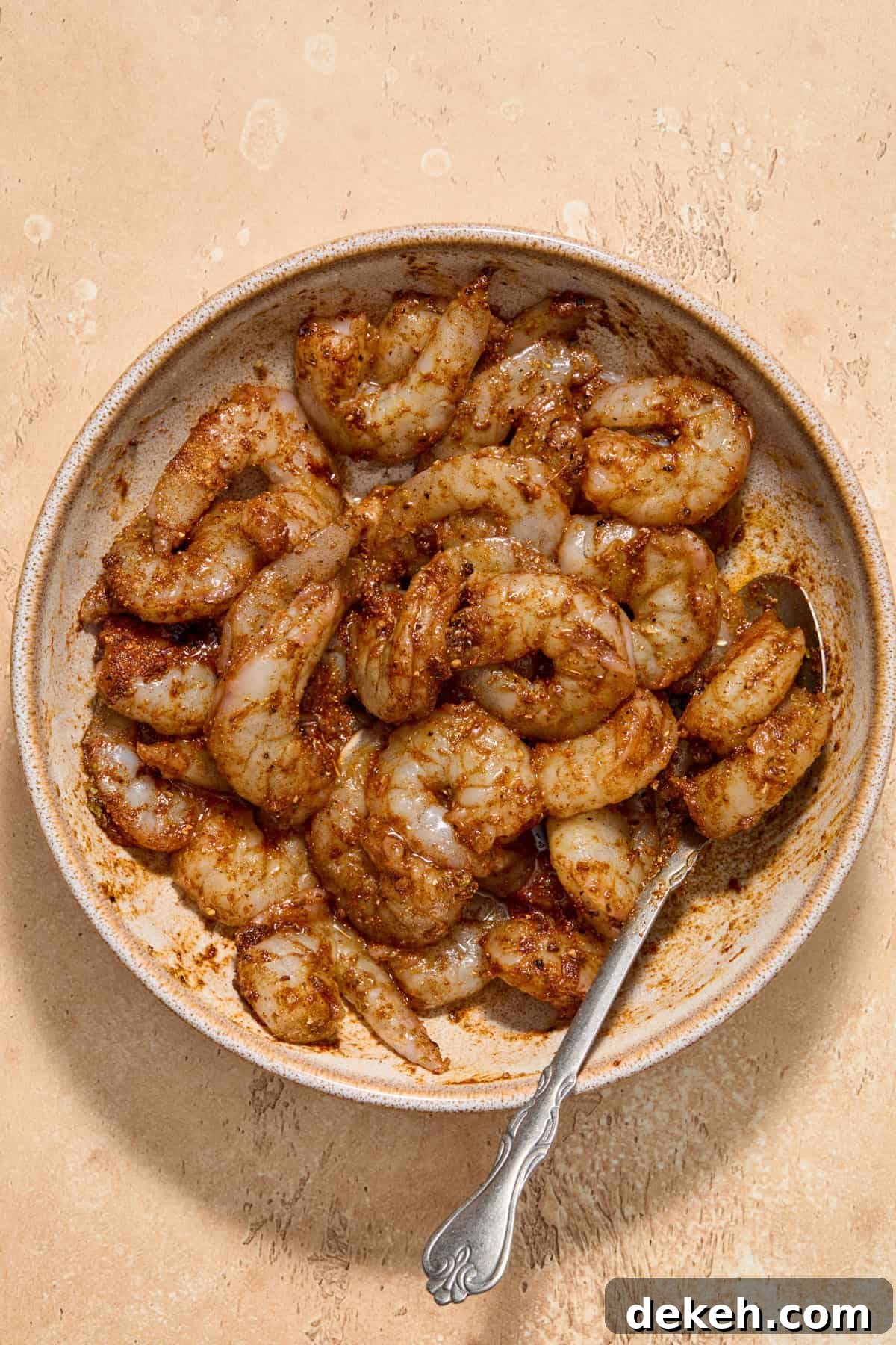 Seasoned shrimp in bowl with spoon before cooking.