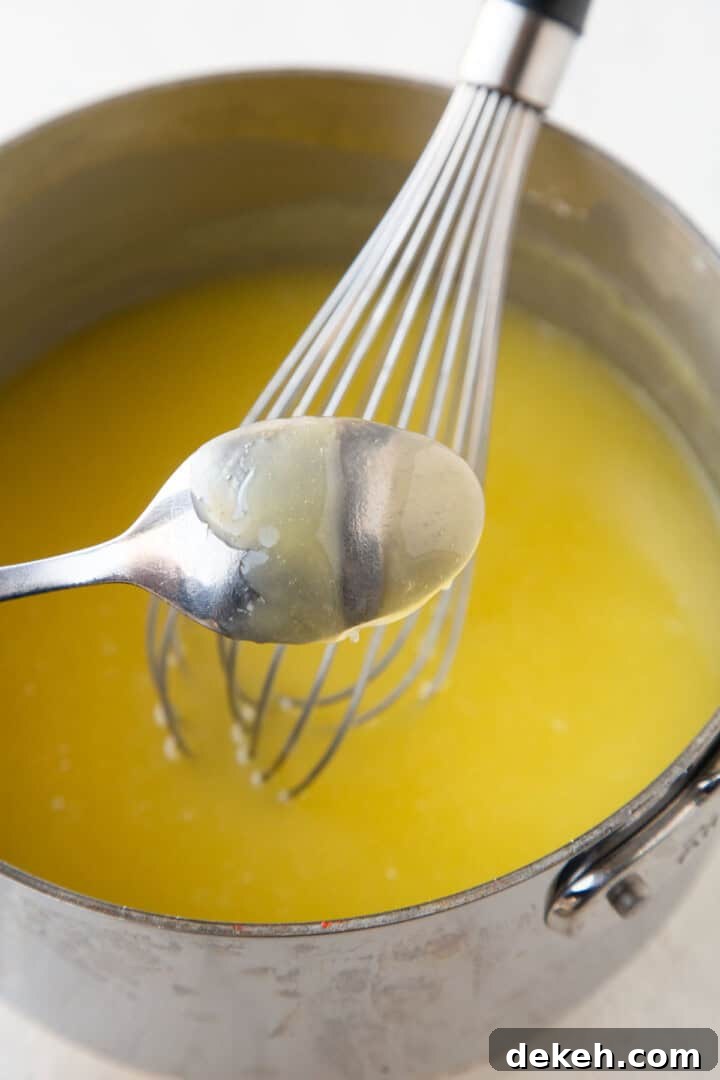 yellow mixture in a saucepan in the background with a spoon with a finger print through the yellow mixture on it.