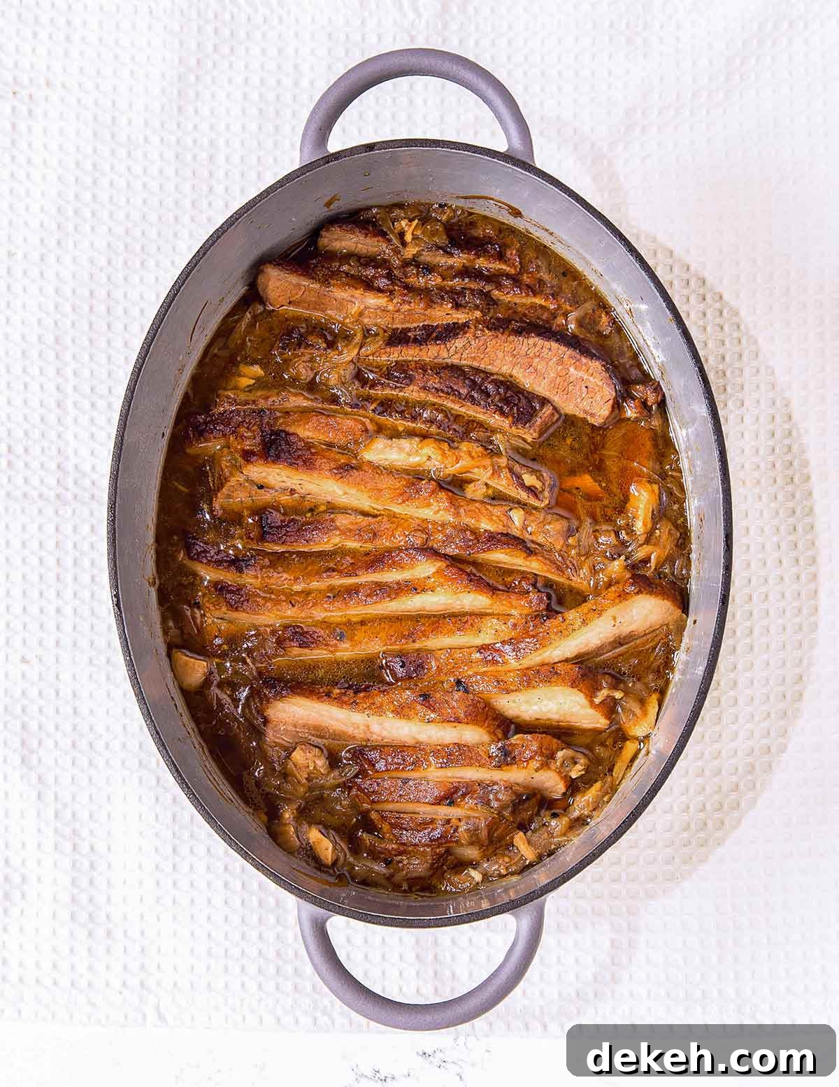 French onion brisket in an oval enamel casserole dish on a white background.