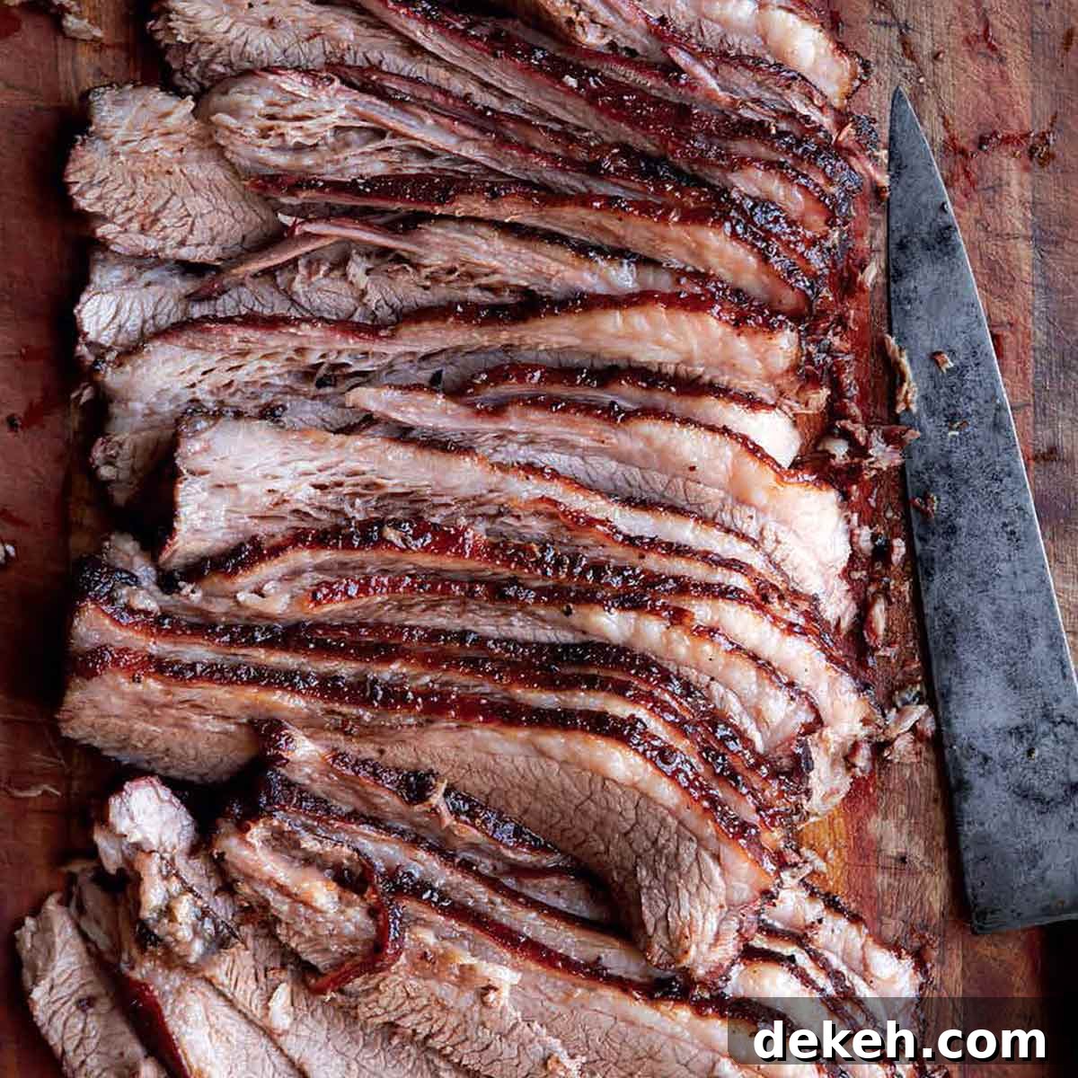 A sliced Texas brisket on a wooden board with a knife lying beside it.