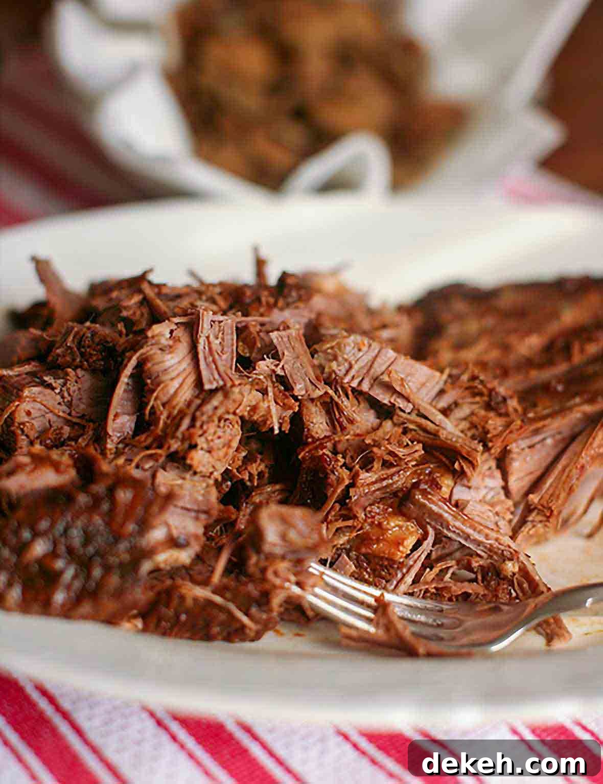 A plate of shredded Coca-Cola brisket with a fork resting in the meat.