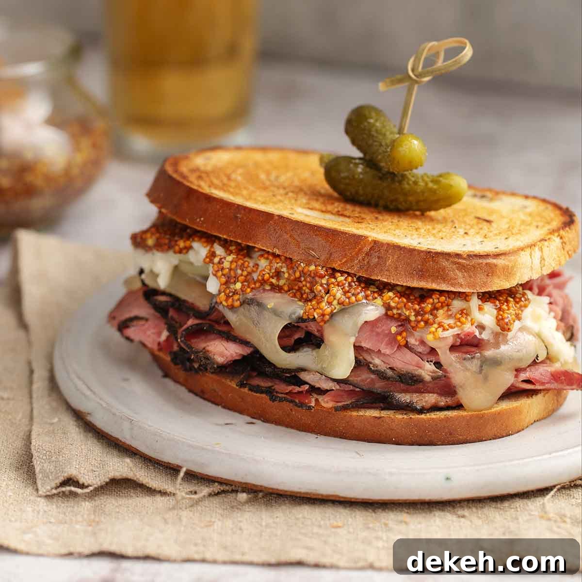 A homemade pastrami sandwich on toasted bread with mustard, cheese, and pickles.