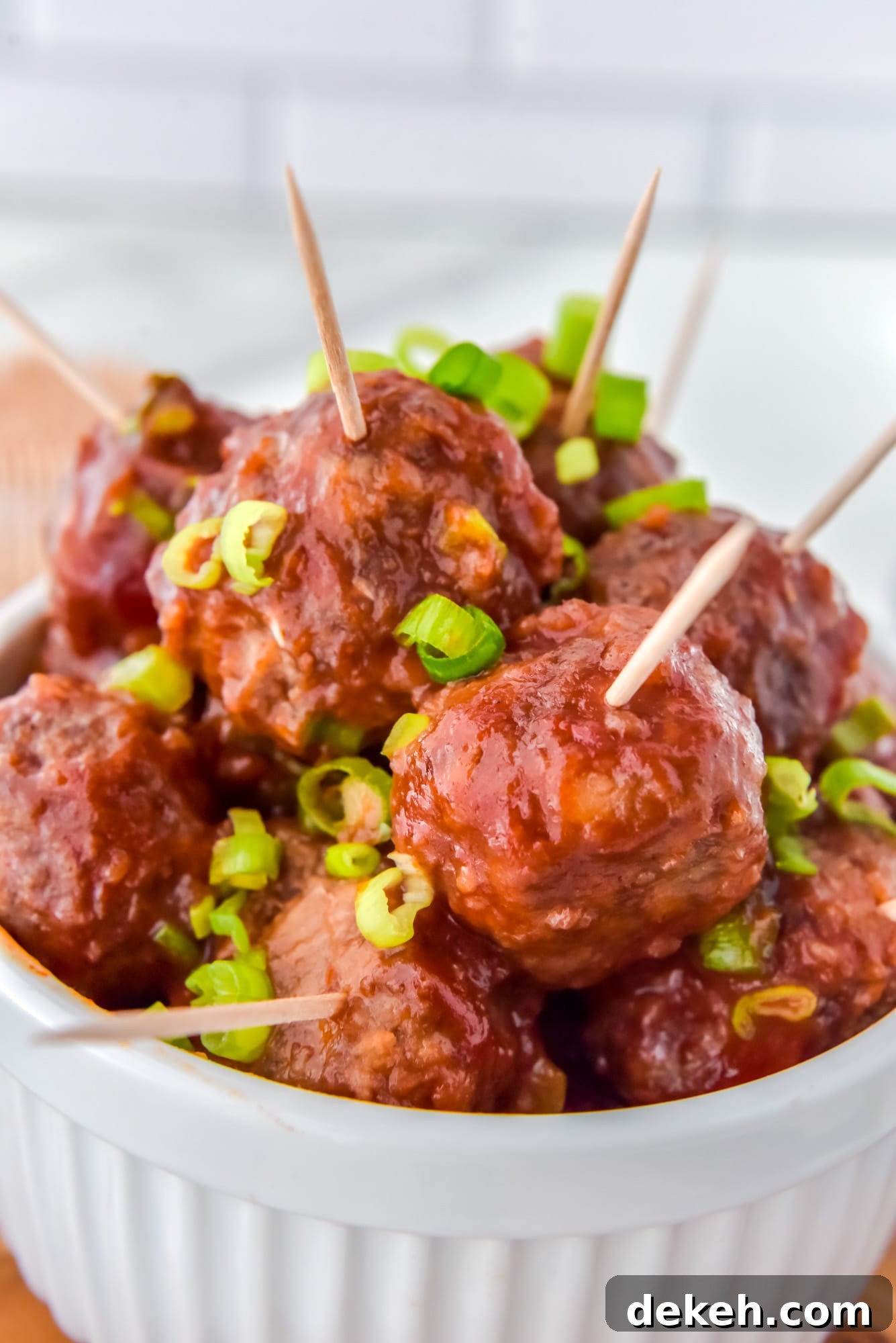 Cranberry meatballs with toothpicks inserted, and garnished with sliced green onions. Served in a white dish.