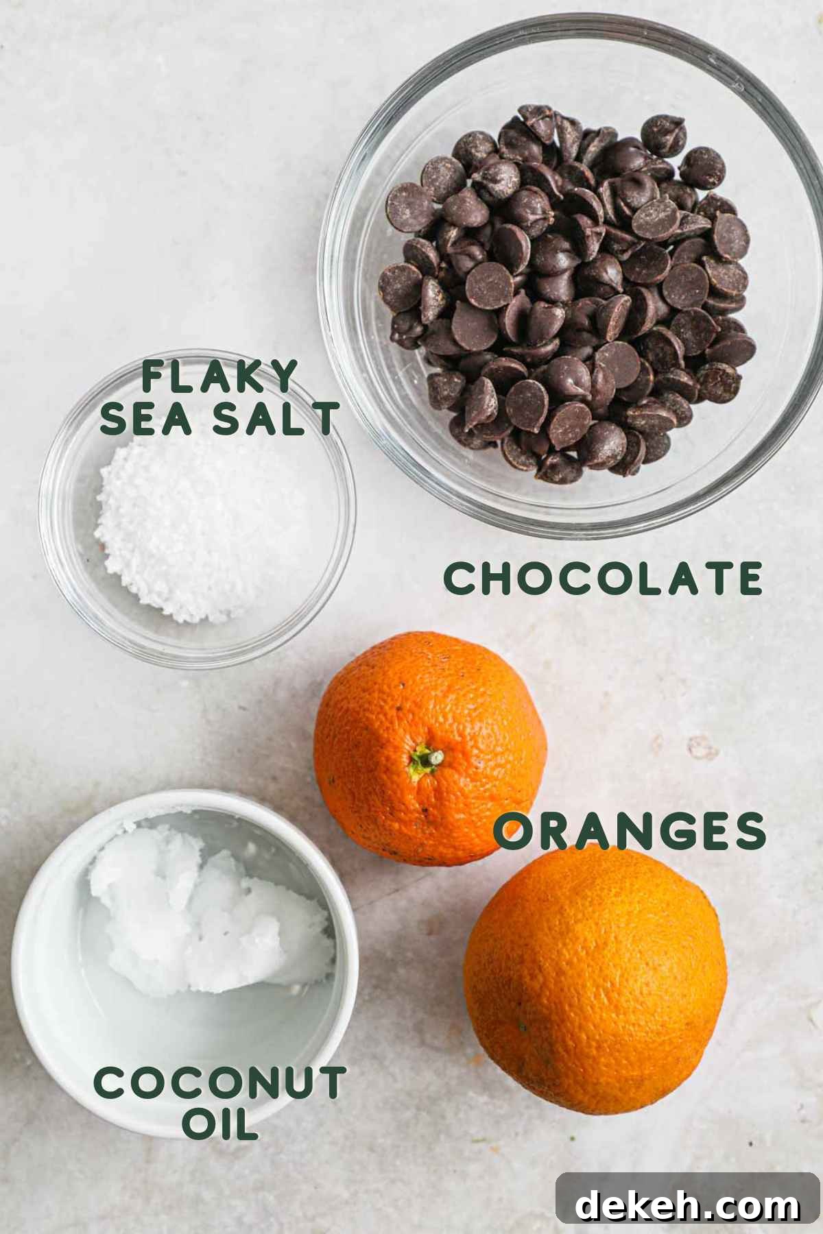 Ingredients to make chocolate-covered mandarin oranges, including chocolate, coconut oil, oranges, and flaky sea salt.