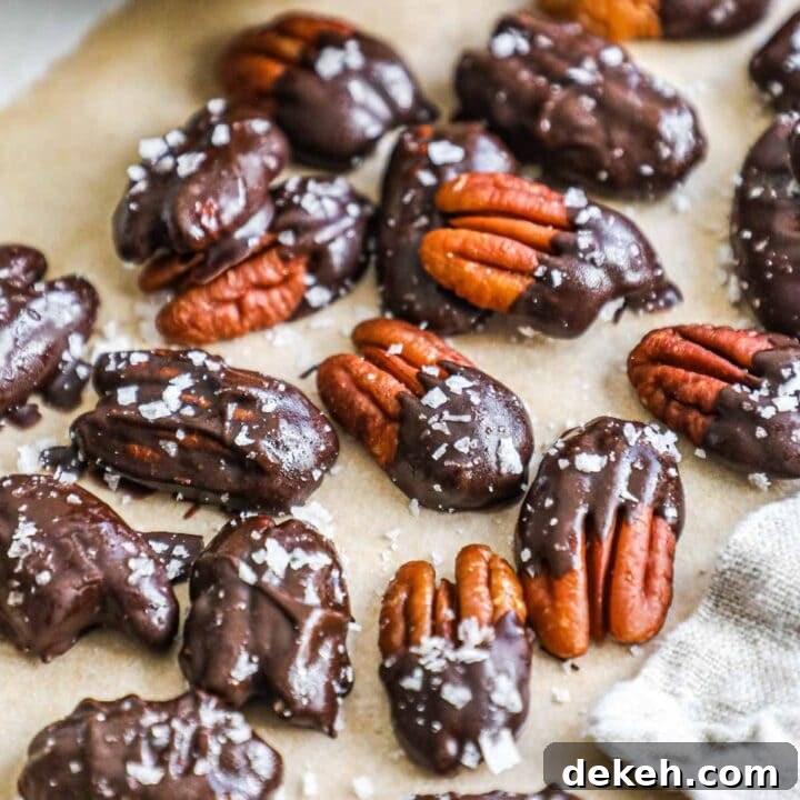 Homemade chocolate-covered pecans with flaky sea salt on a sheet of parchment paper.