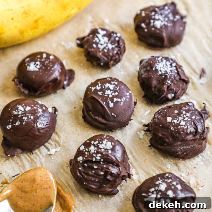 Frozen chocolate-covered banana bites with peanut butter and flaky sea salt on a parchment paper-lined baking sheet.