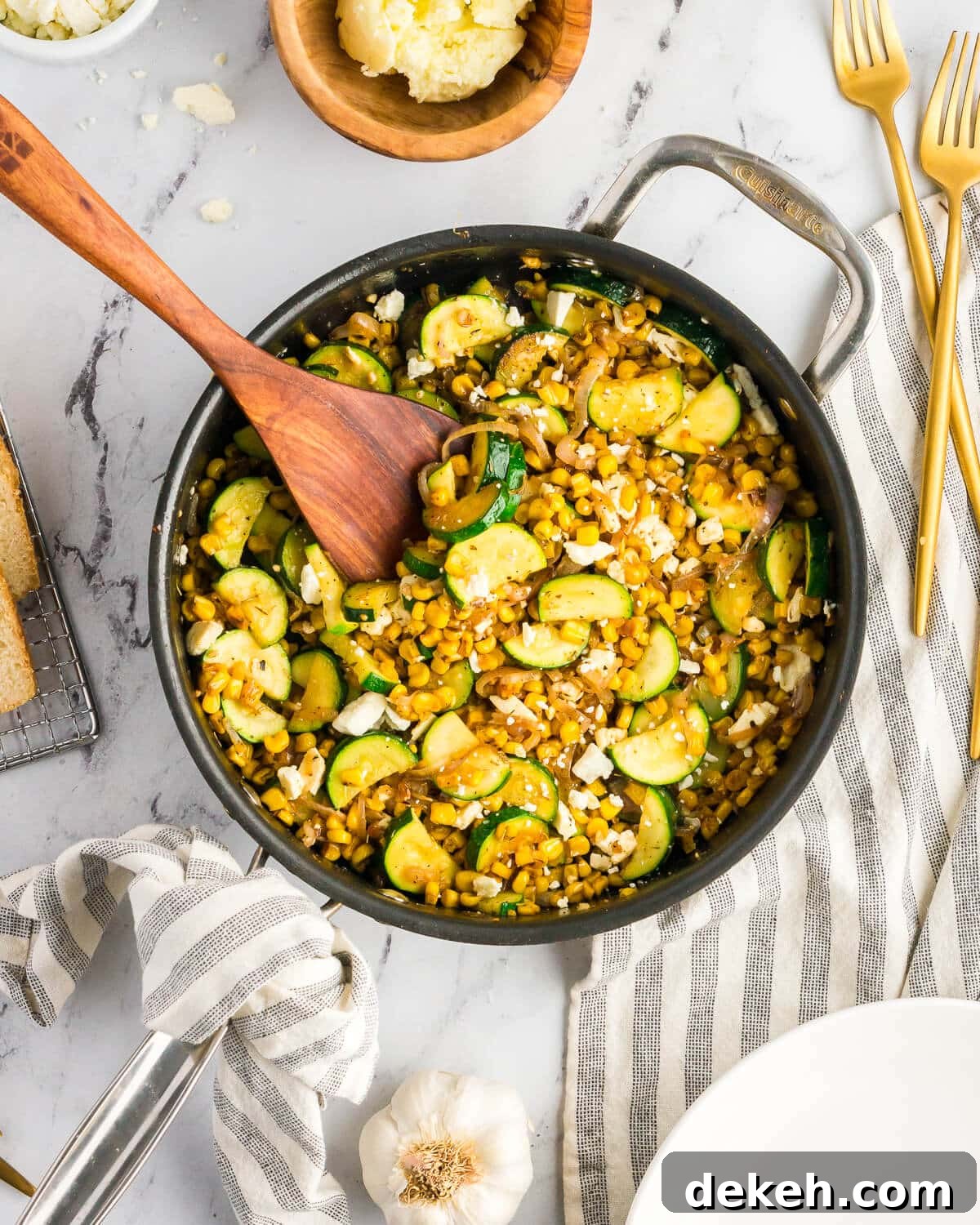 a skillet with caramelized corn, shallots, zucchini, and feta with a wooden spoon in it. 