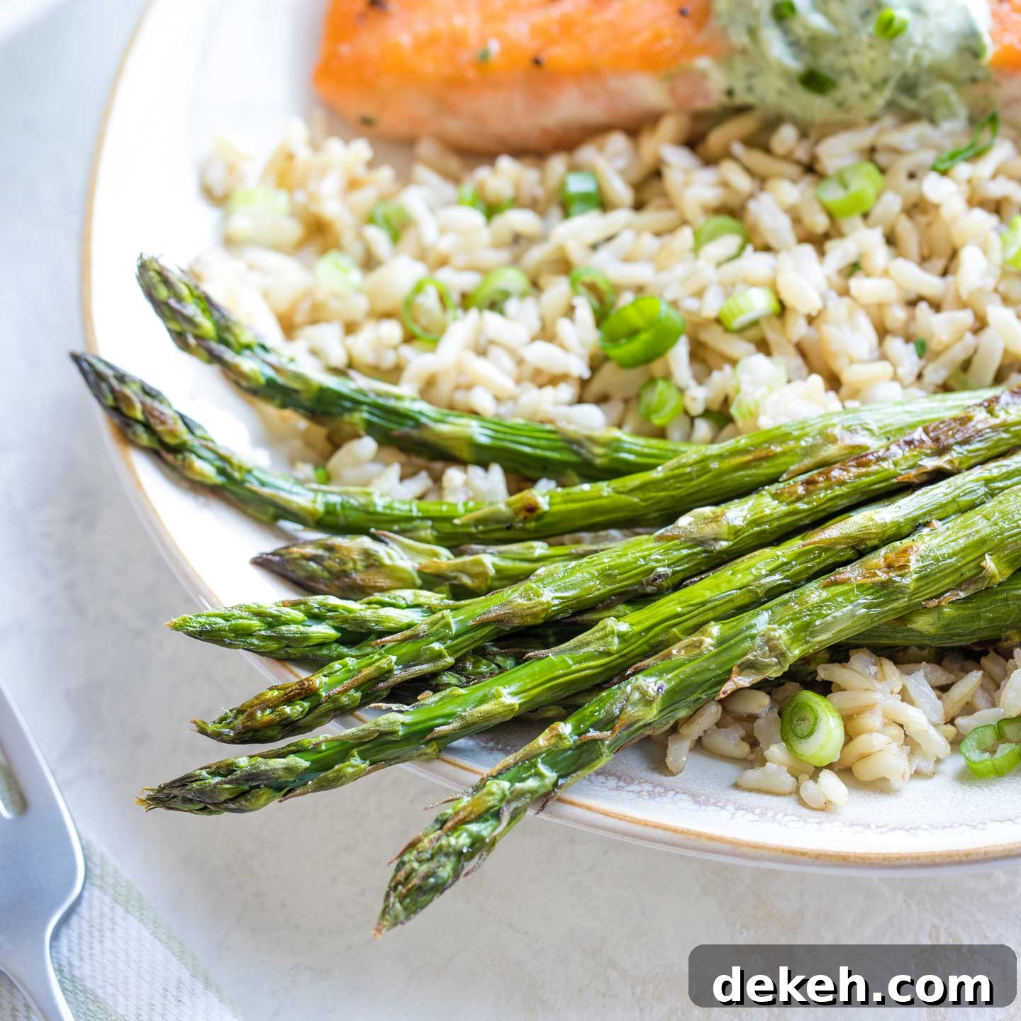 Hero photo of a serving portion of roasted asparagus spears served with rice and salmon, with a green-striped napkin and fork visible alongside.