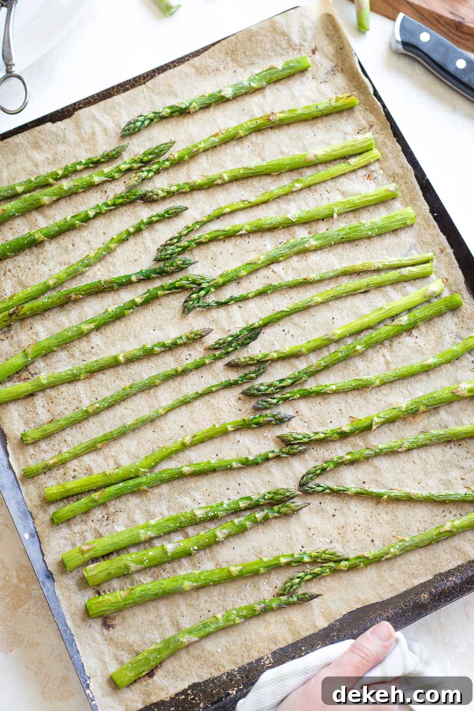 A hand holding the edge of the baking pan just after the asparagus has finished roasting and been taken from the oven.