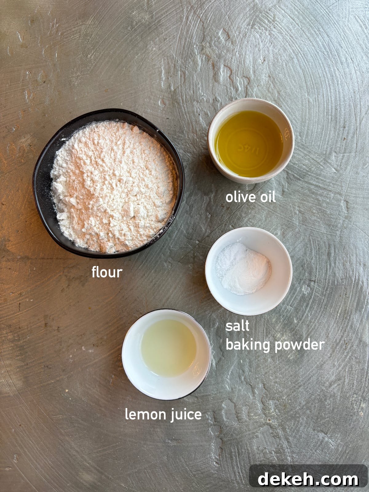 overhead shot of the ingredients needed to make the dough for Fatayer Spinach Pies. Each ingredient is in a small bowl and labeled with white text. 