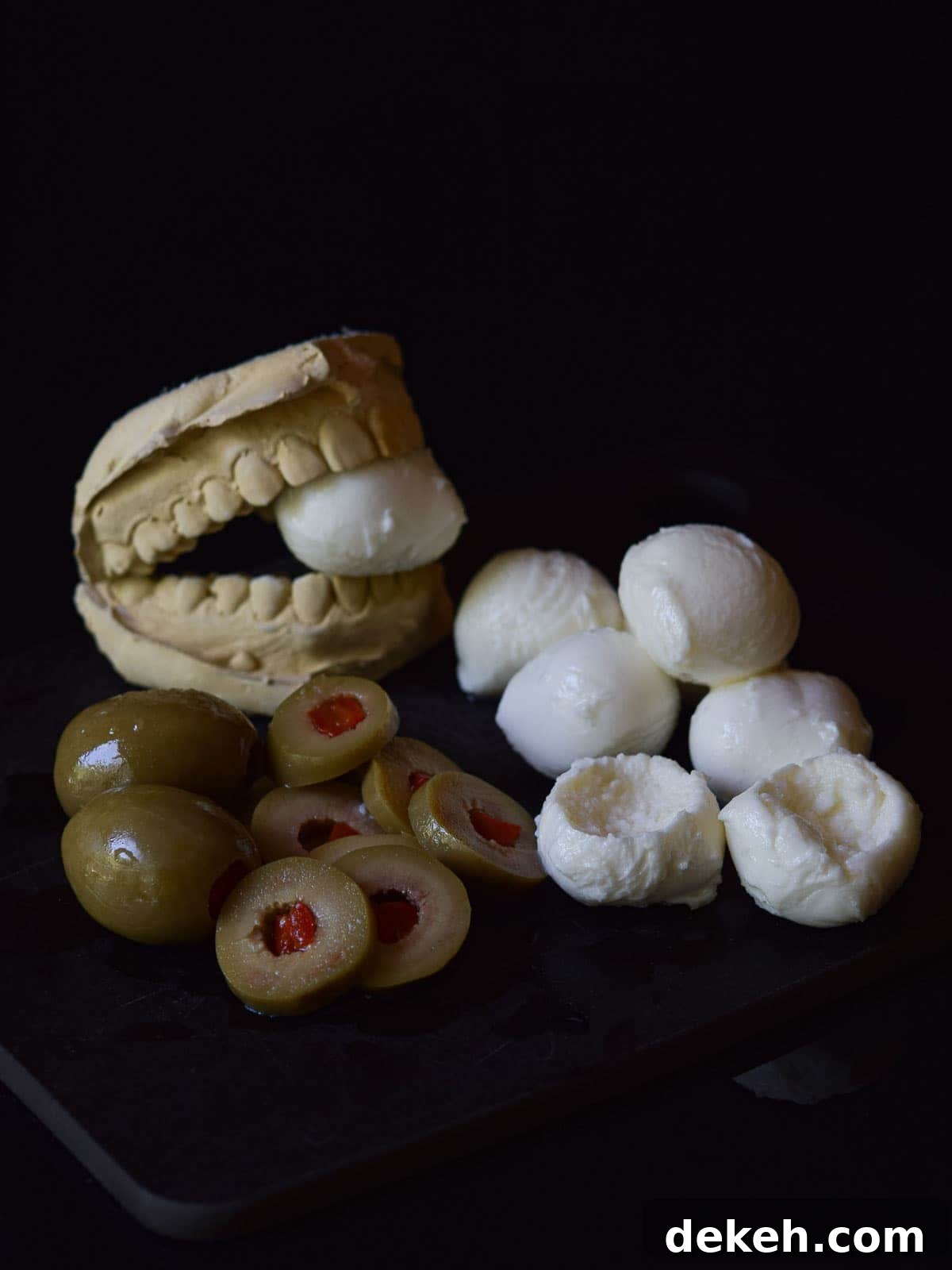 Mozzarella balls with olives, with a scoop taken out on black surface.