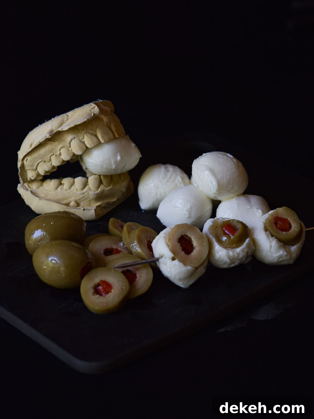 Mozzarella eyeballs on a skewer on a black surface.