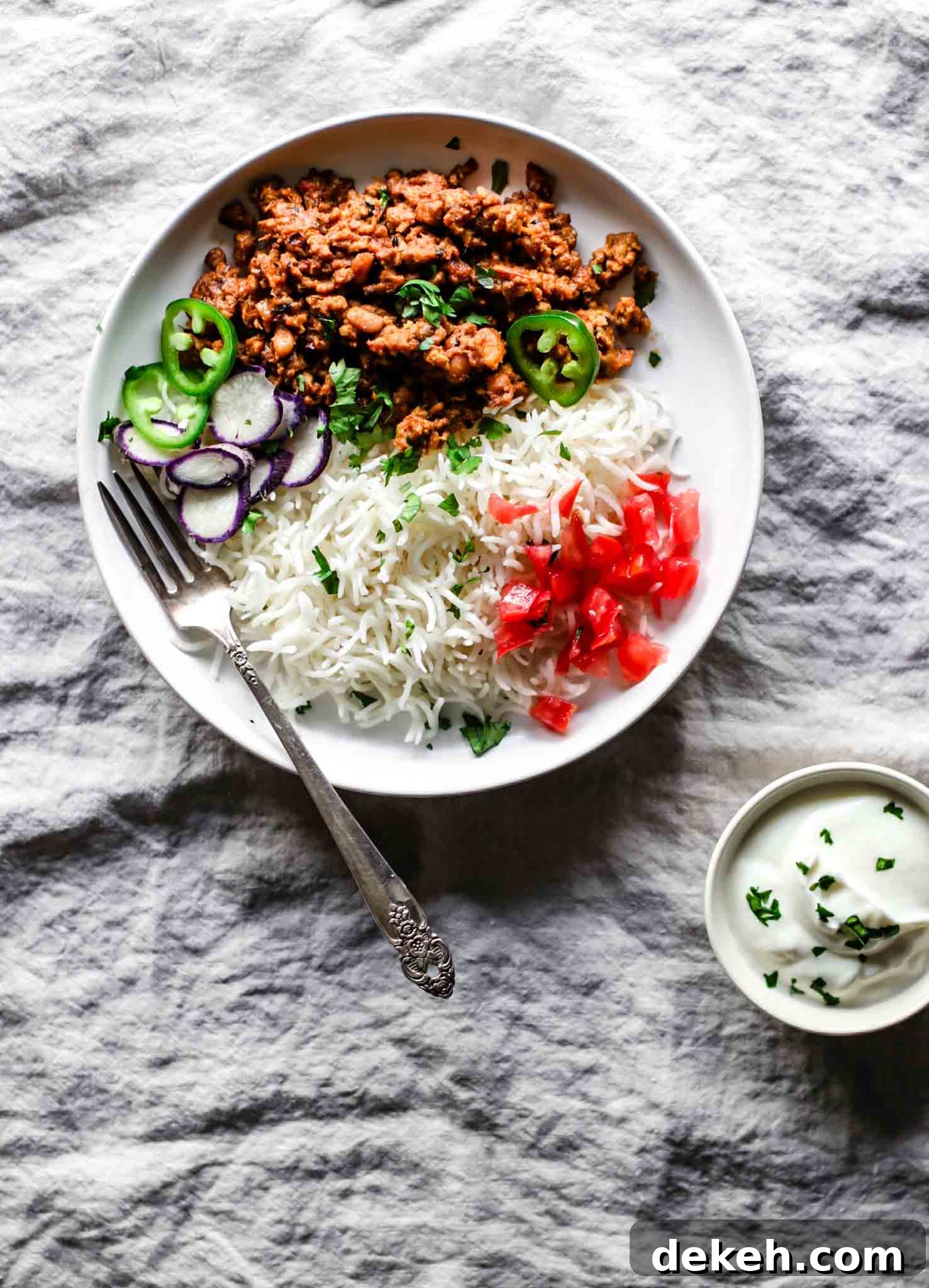 Keema Lobia on a white plate with a silver fork with rice, vegetables, and yogurt on the side