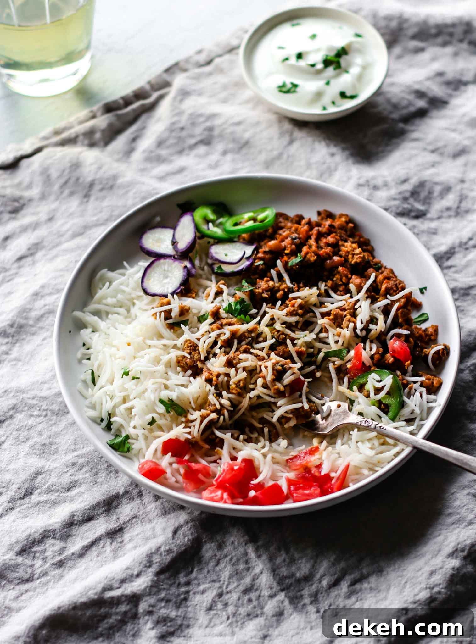 Keema Lobia mixed with rice on a white plate with a silver fork, vegetables, and yogurt on the side