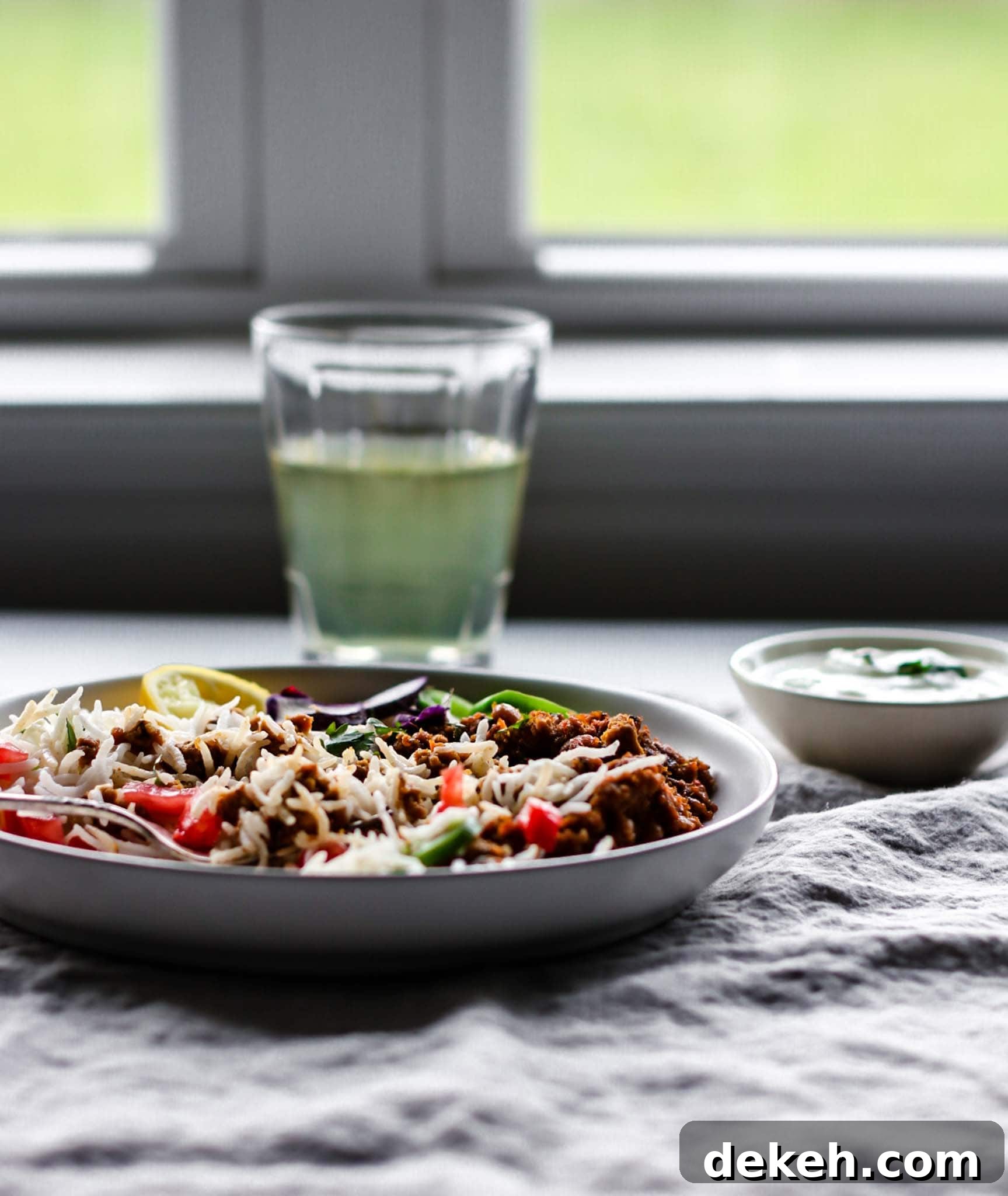 A plate of Keema Lobia with a silver fork with rice, vegetables placed in front of a window.