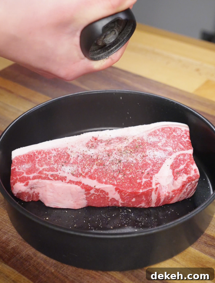 Raw sirloin steak being seasoned generously with salt and black pepper before cooking for Crying Tiger Steak.