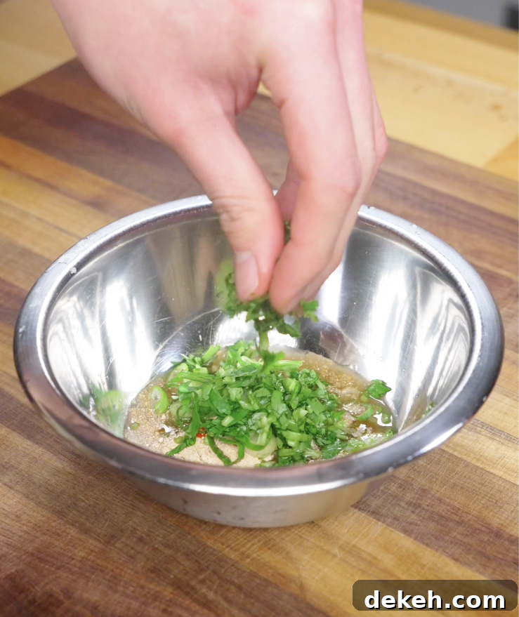 Finely chopped cilantro being added to a bowl of Crying Tiger Steak sauce to build a fresh, herbal flavor.