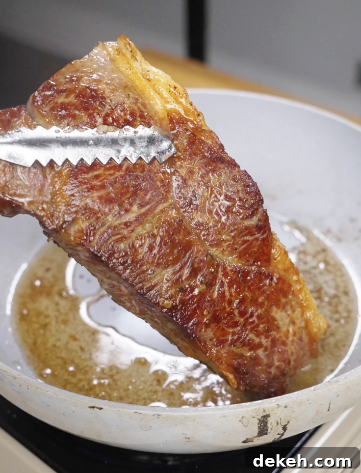 Steak being seared in a hot pan with oil, developing a deep golden crust as the first step in making Crying Tiger Steak.