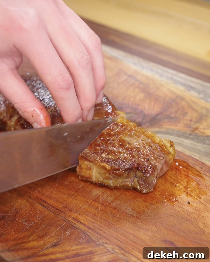 Cooked Crying Tiger Steak being sliced thinly against the grain on a wooden cutting board for optimal tenderness.
