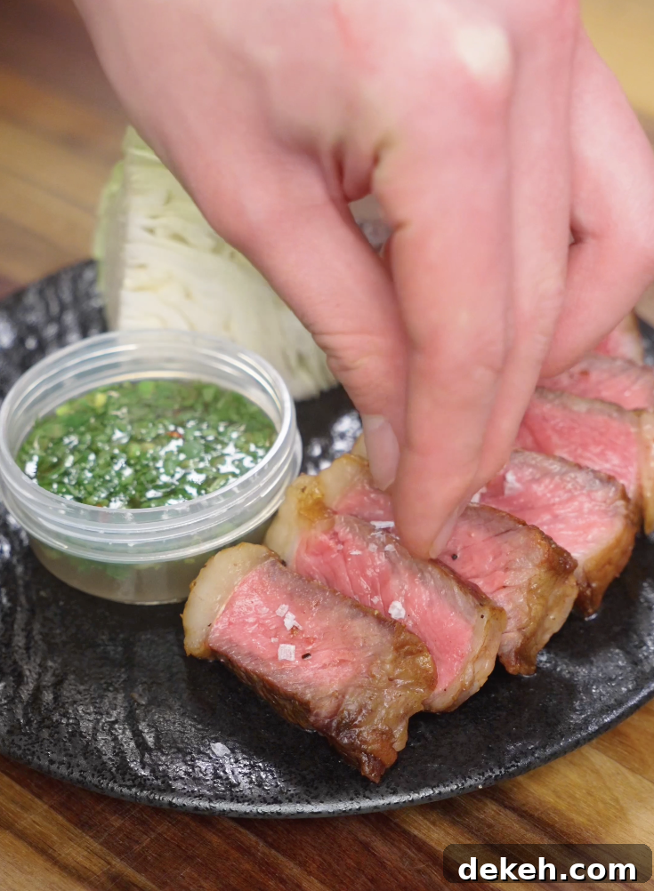 Flaky salt being sprinkled over sliced Crying Tiger Steak just before serving to enhance flavor and texture.