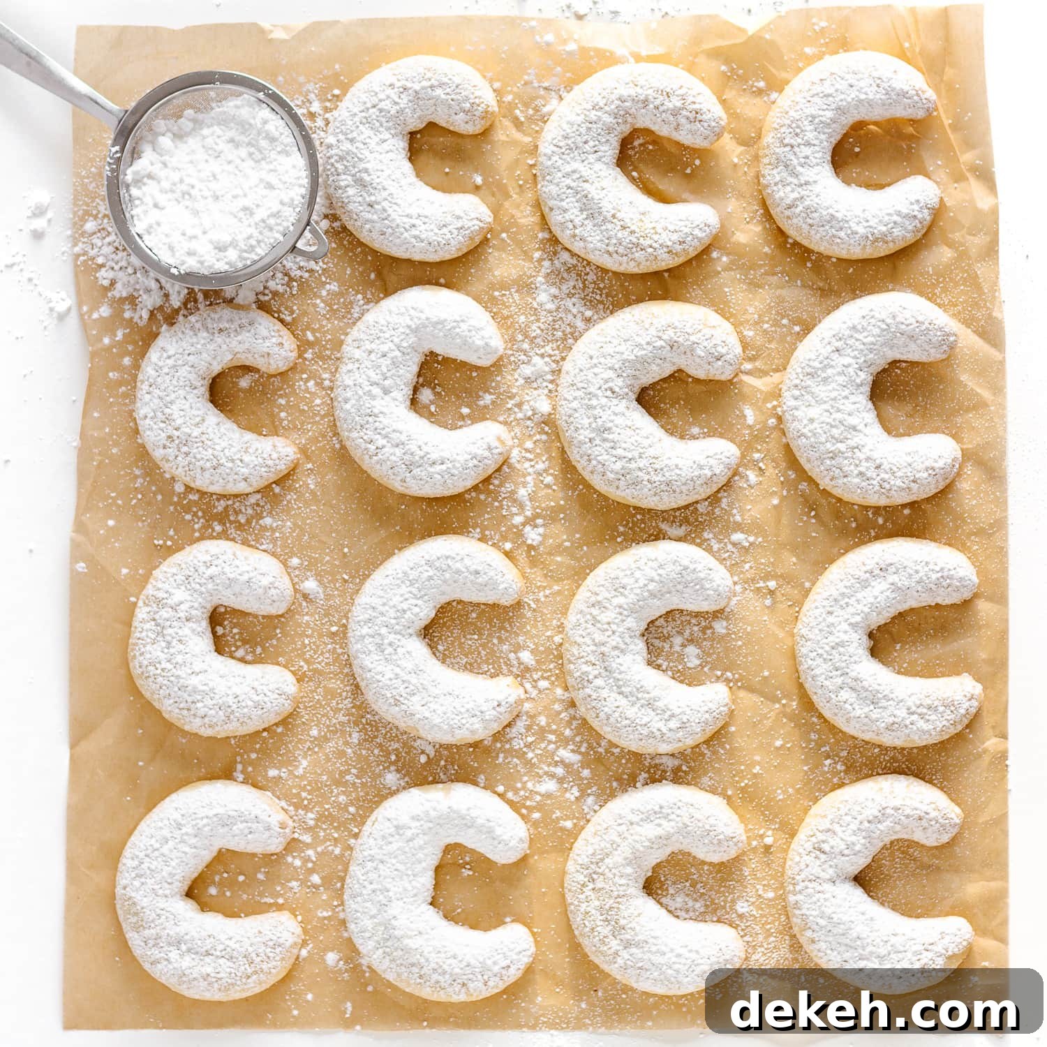 Vanillekipferln (vanilla almond crescent cookies) dusted with powdered sugar and lined up on a square piece of parchment paper.