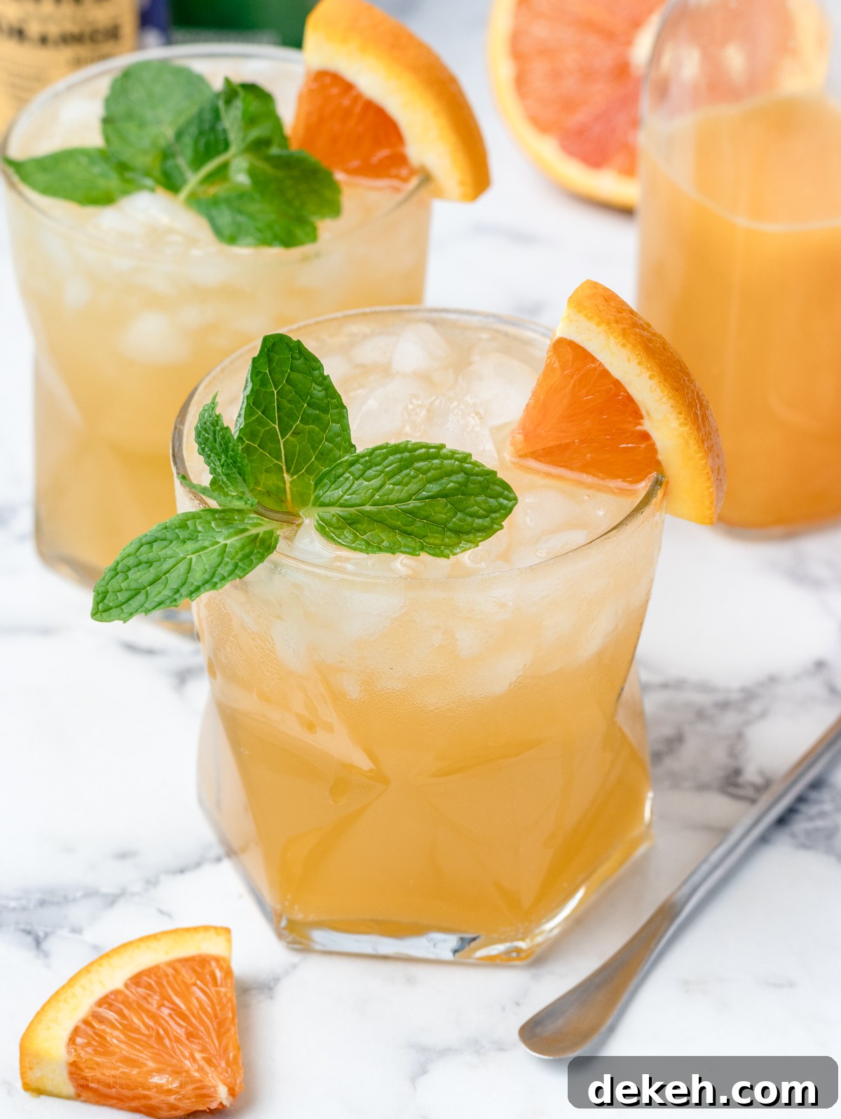 2 glasses of orange coconut water mocktail garnished with mint leaves and orange wedges.