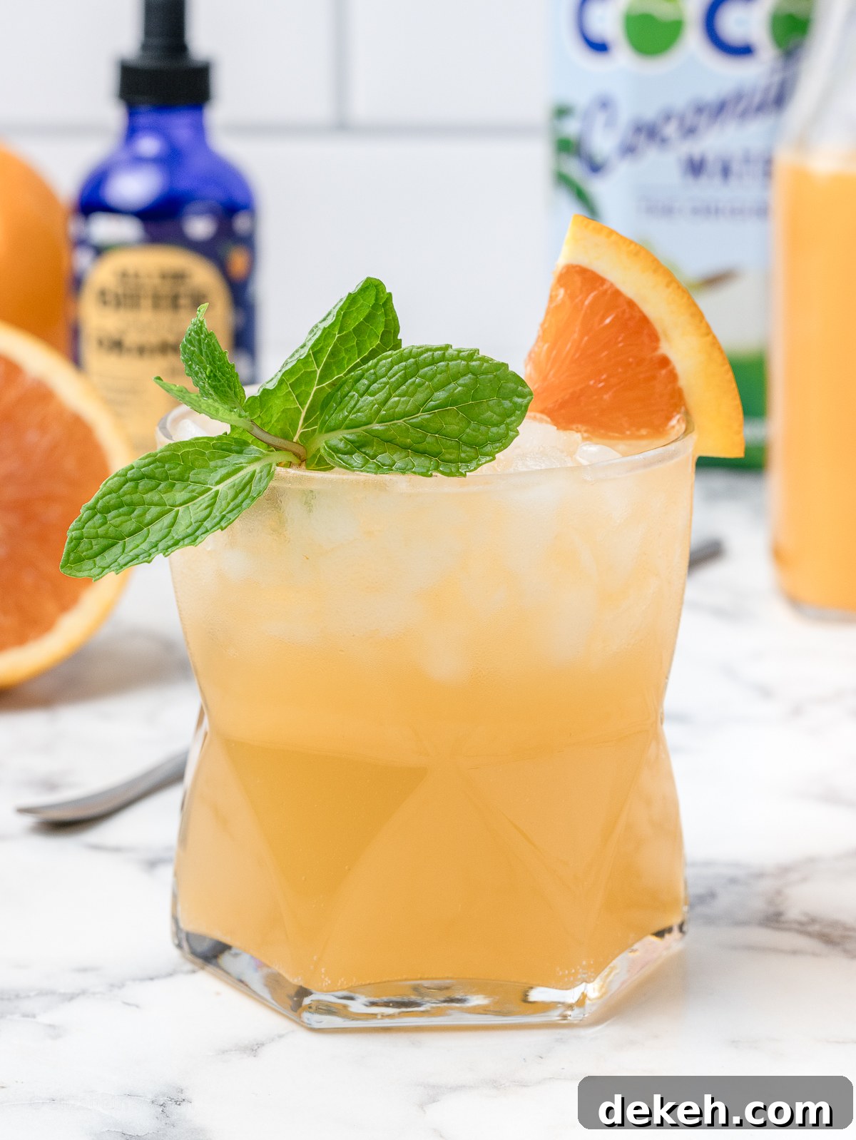 A refreshing coconut and orange mocktail with orange bitters, coconut water, and freshly squeezed orange juice in the background.