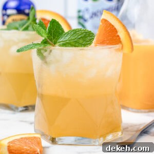 An iced Orange Coconut Water Mocktail with fresh mint and orange slices. They are a light and refreshing orange color.