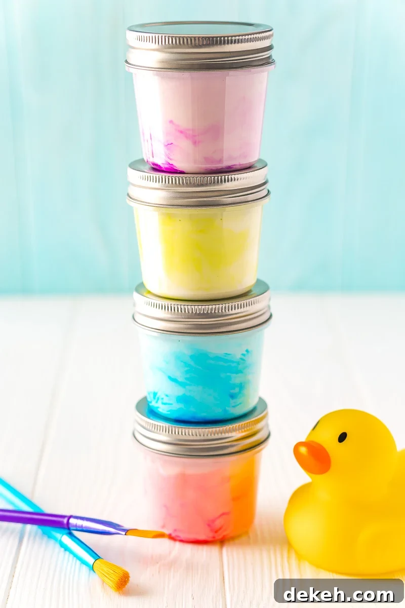Small jars of paint stacked on top of each other with a rubber ducky and paint brushes sitting next to them on a white table.