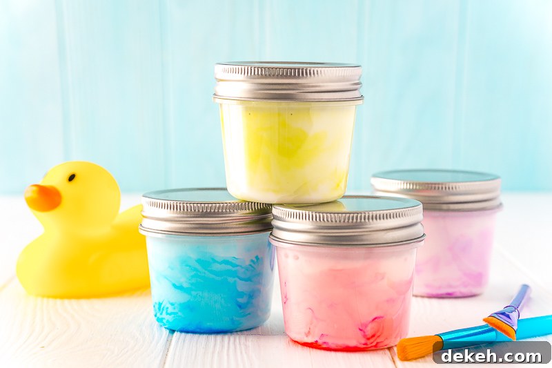 Small jars of paint stacked on top of each other with a rubber ducky and paint brushes sitting next to them on a white table.