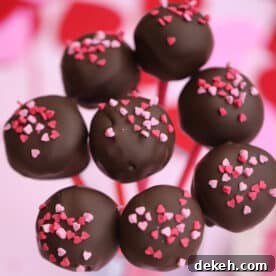 Chocolate-covered gluten free cake pops with heart sprinkles on top, against a pink background.