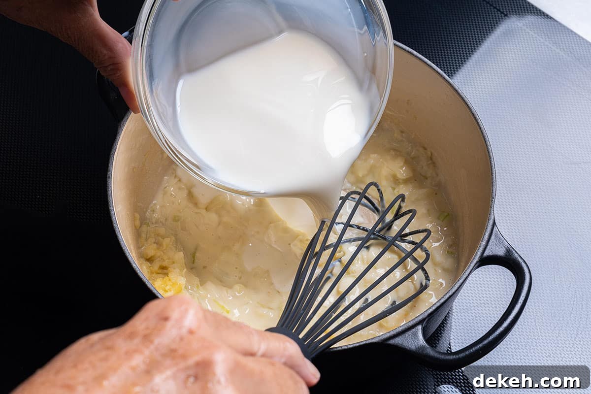 pot with flour, garlic and onion having milk poured in
