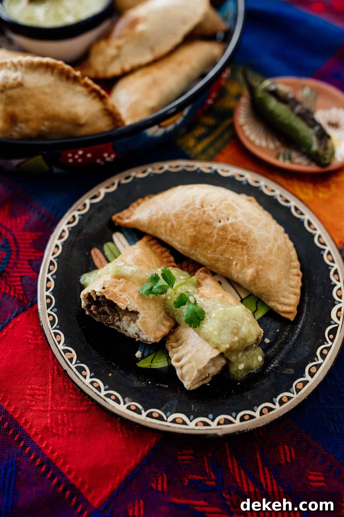 open empanada on a Mexican black plate filled with Mexican picadillo drizzled with salsa verde.