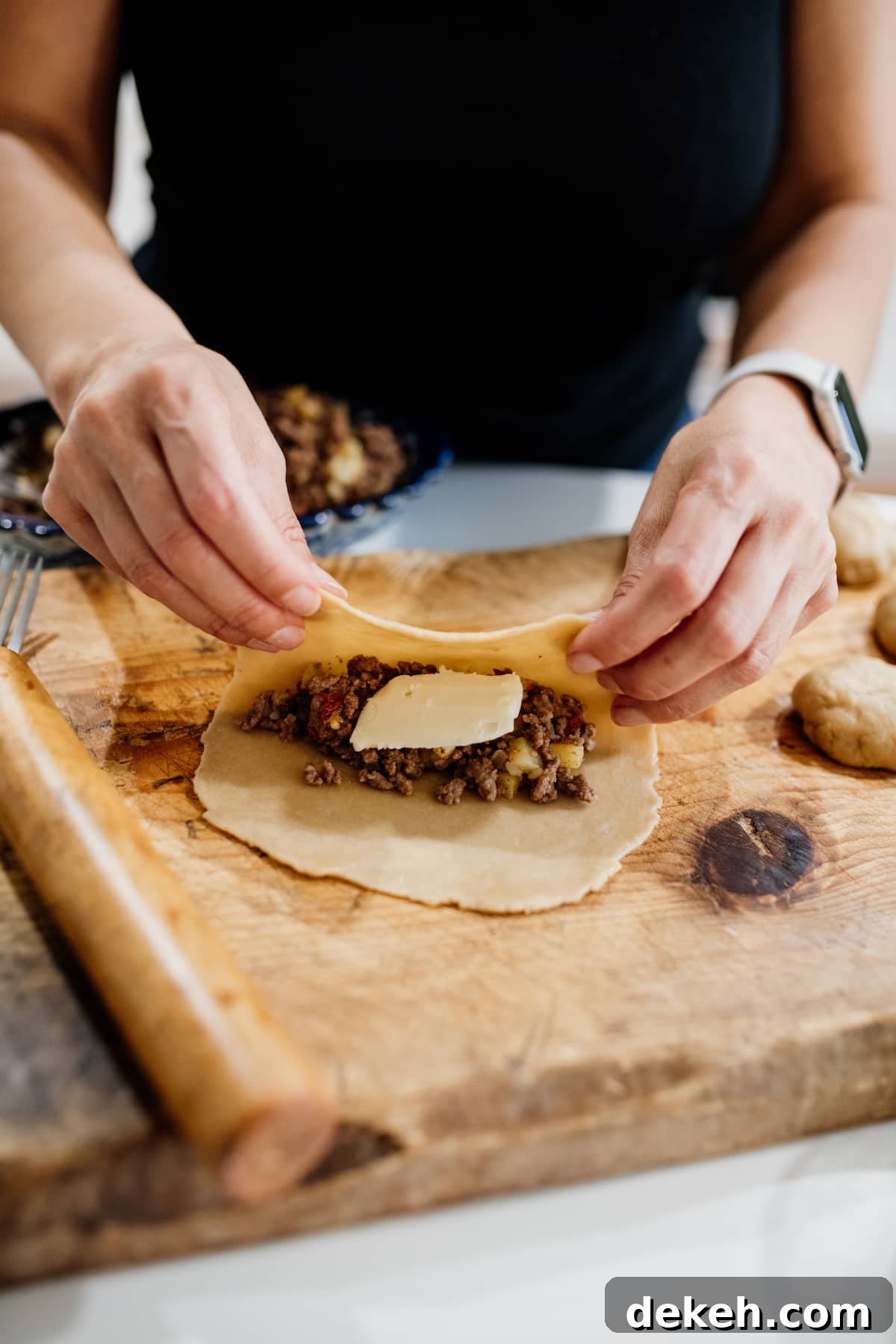 empanada disk being filled with picadillo and a slice of cheese and folded over with hands.