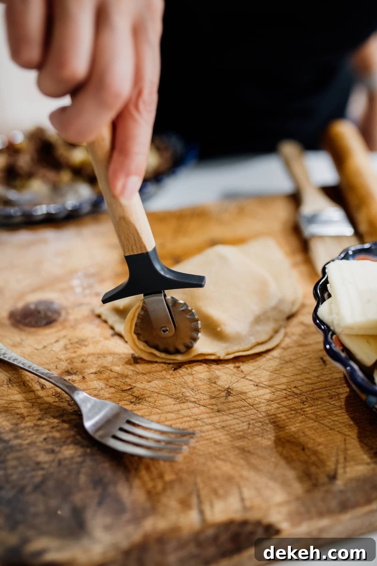 pastry cutter trimming dough for empanadas on a wooden cutting board.