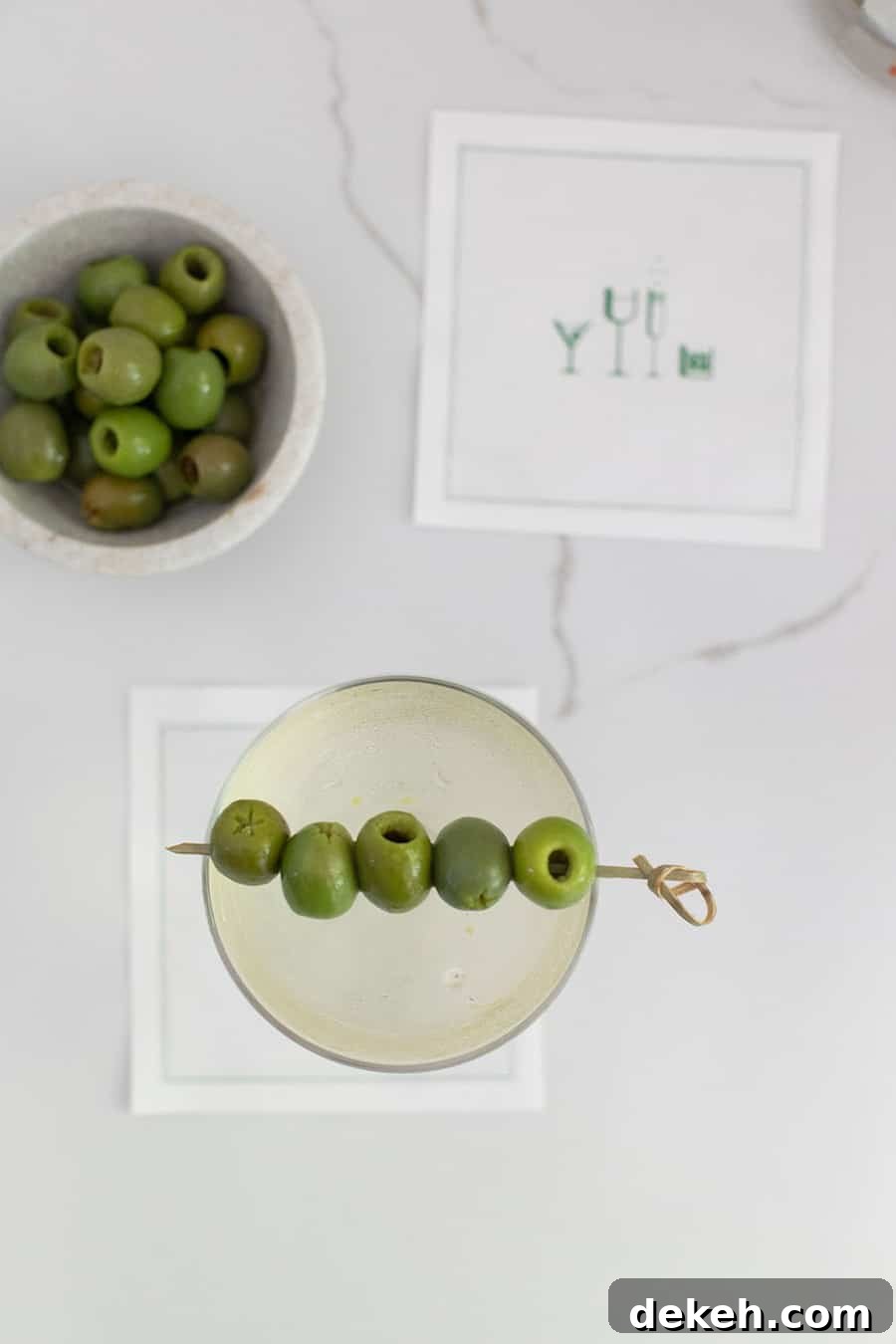 Dirty martini on a cocktail napkin with a bowl of olives.