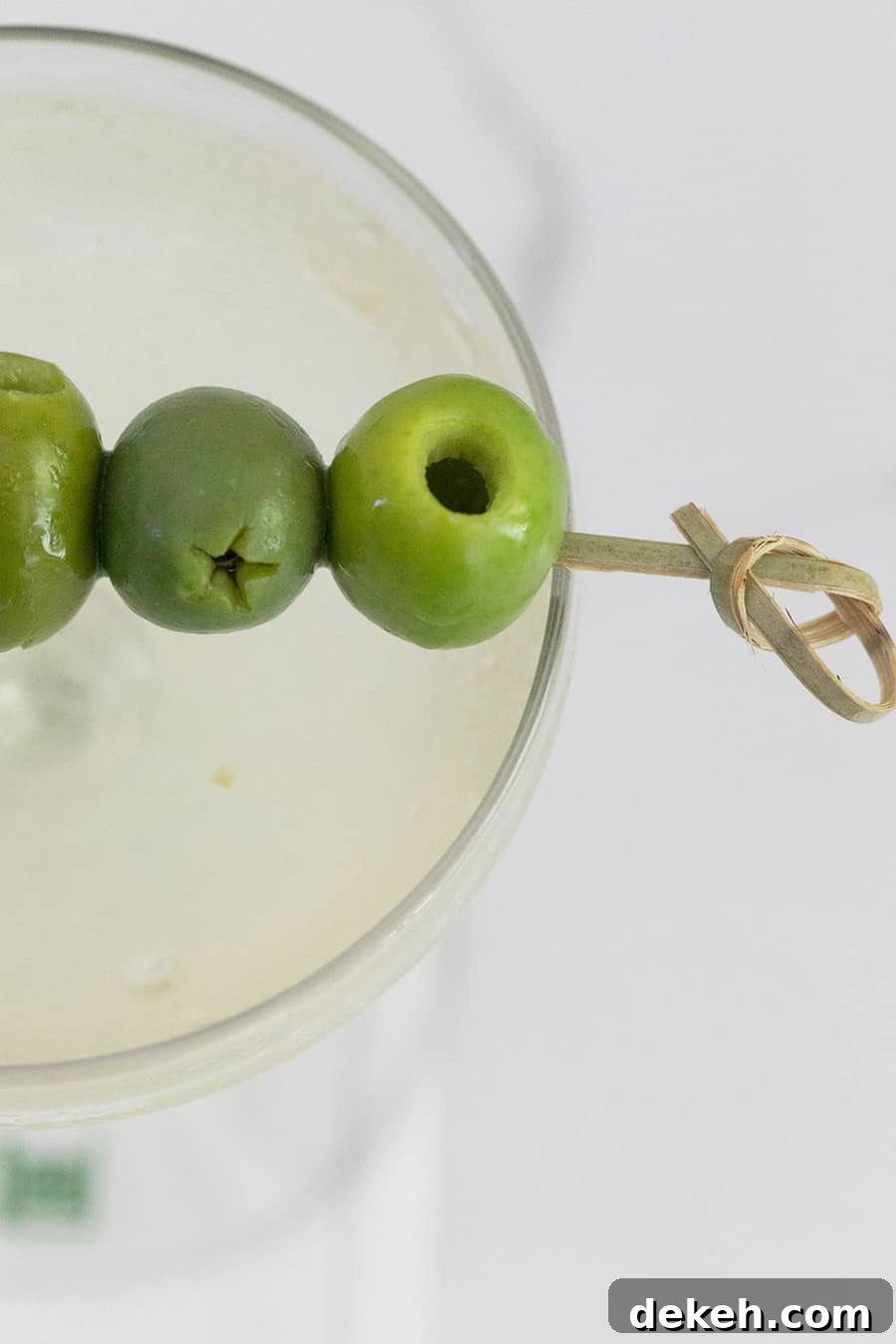 Green olives on a pick laying over a dirty martini.