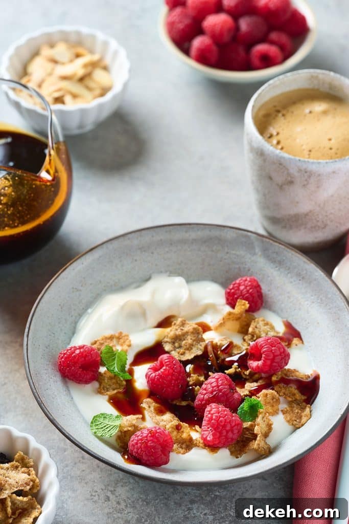 Yogurt in a bowl garnished with fresh raspberries, mint, granola, and homemade date syrup.