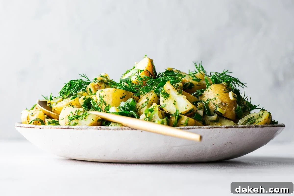 Side view of a potato salad without mayonnaise, eggs, or celery. The salad is in a ceramic bowl with a gold serving spoon.