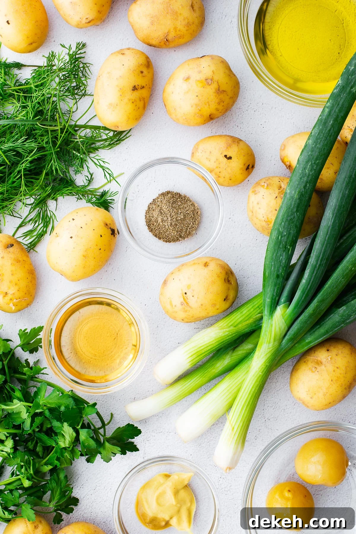 Raw ingredients for a no-mayo, no-egg potato salad viewed from above, including celery salt, spring onions, herbs, olive oil, and preserved lemons.