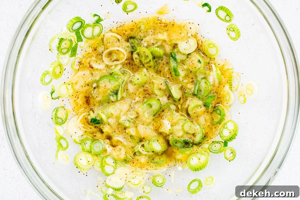 A zesty dressing of preserved lemon, apple cider vinegar, dijon mustard, celery salt, olive oil and sliced spring onions viewed top down in a glass bowl.