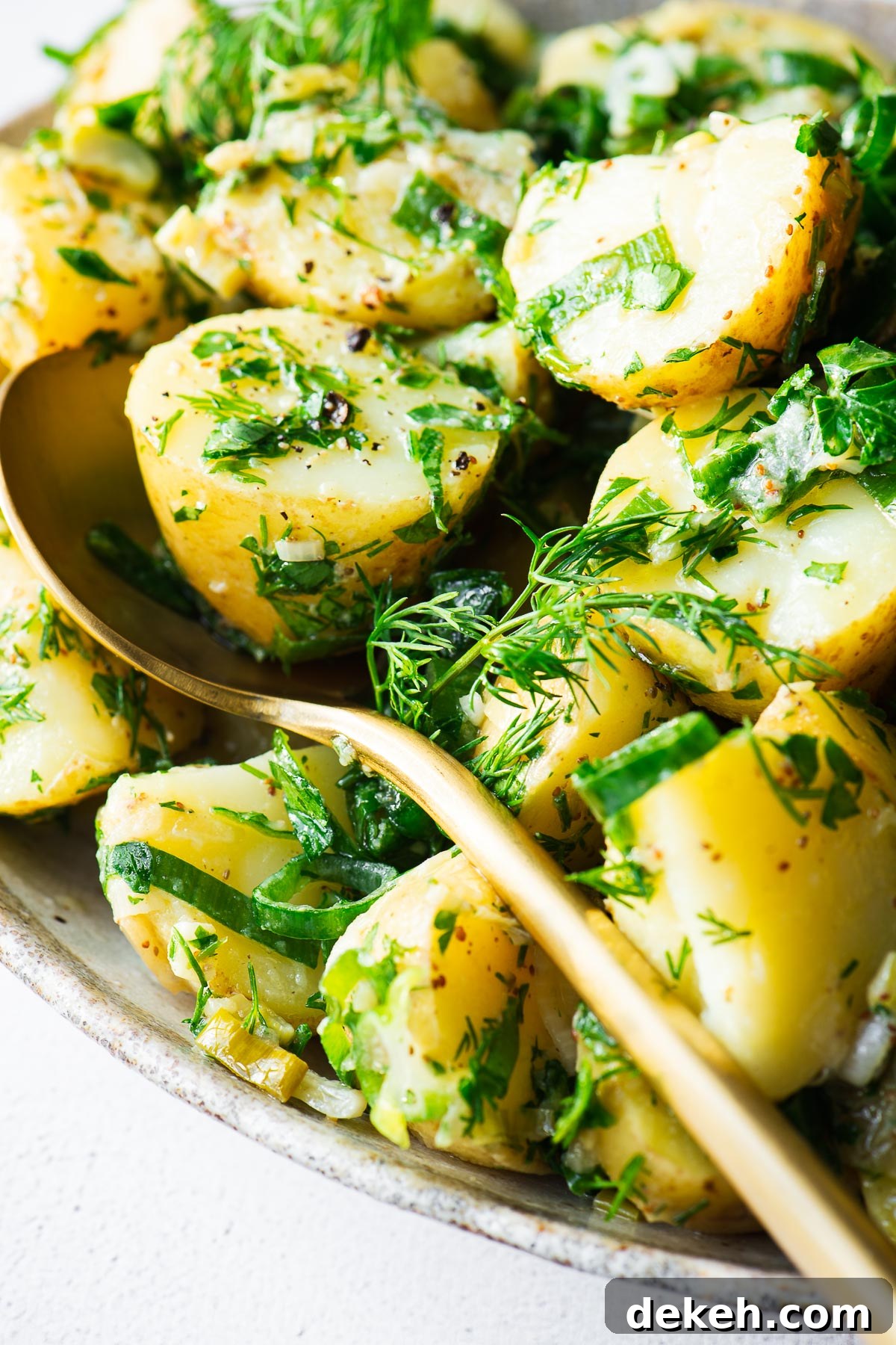 A close-up of herbed potato salad with a gold serving spoon.